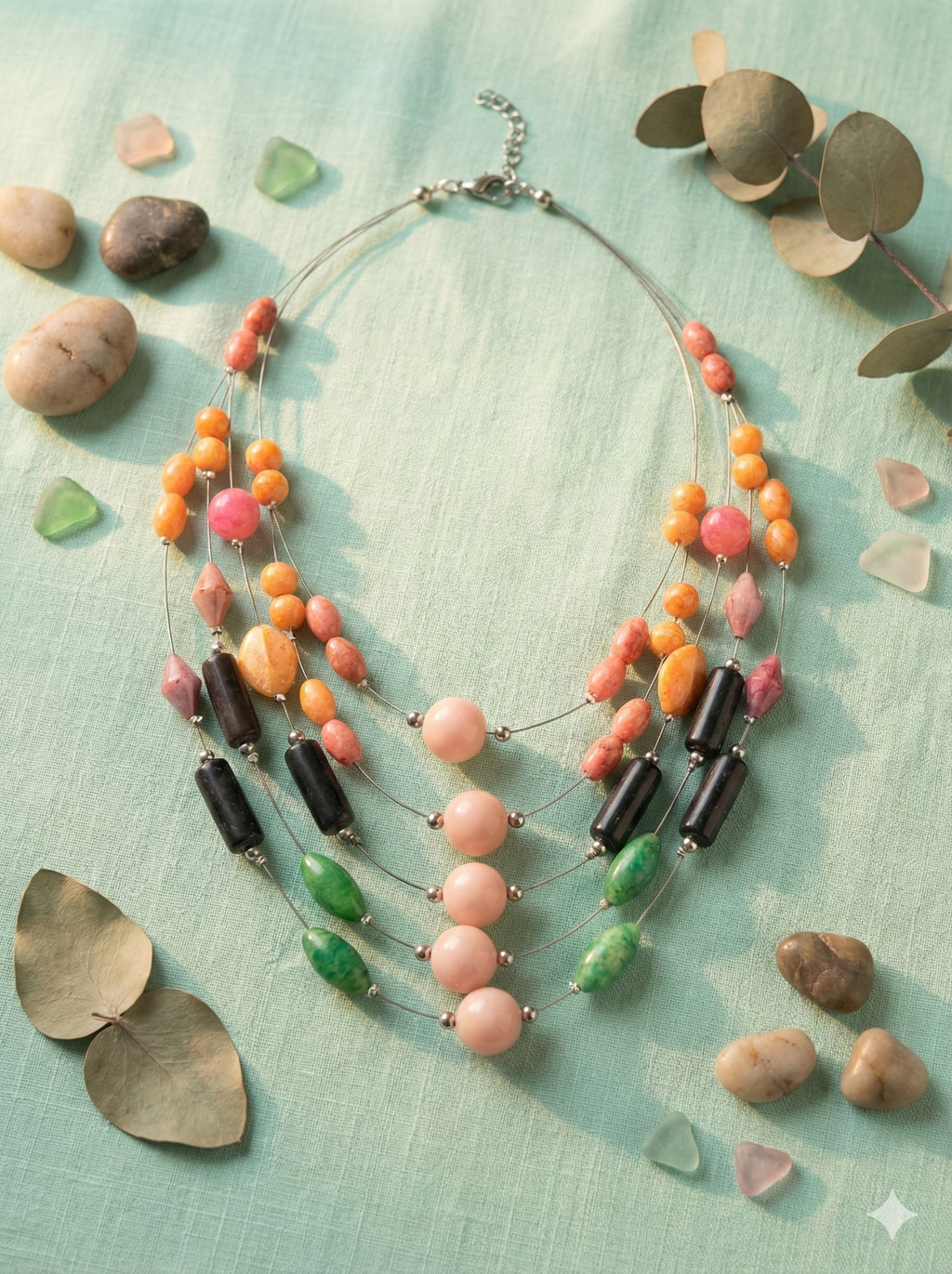 A five-strand tiered necklace featuring large pink central beads, black cylinders, and green accents on silver wire