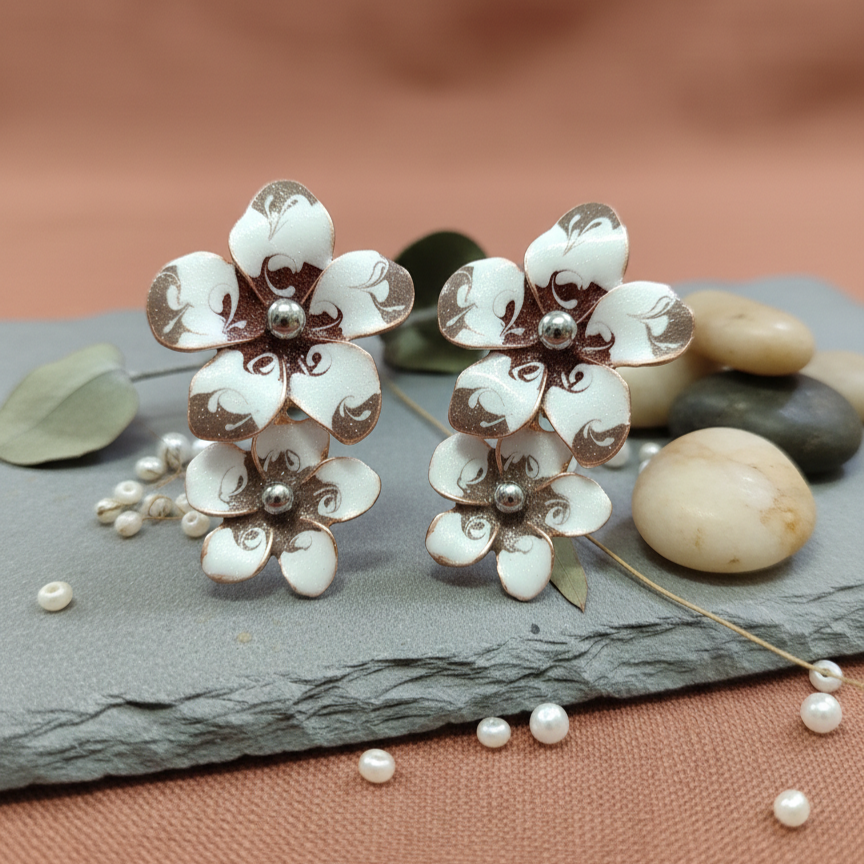 A pair of tiered floral earrings featuring white enamel petals with intricate brown swirl patterns and silver centers