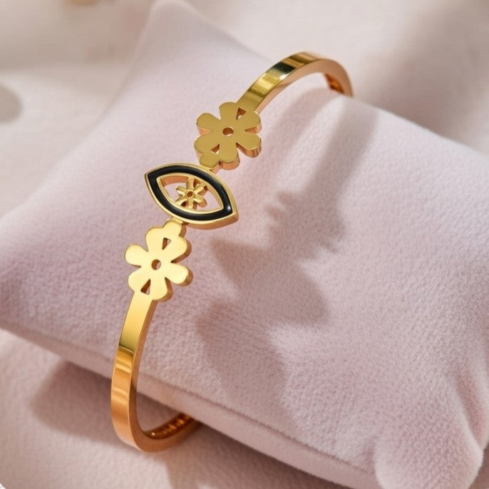 A sleek gold bangle featuring a central black enamel evil eye motif flanked by two gold flower charms