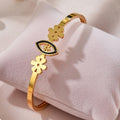 A sleek gold bangle featuring a central black enamel evil eye motif flanked by two gold flower charms