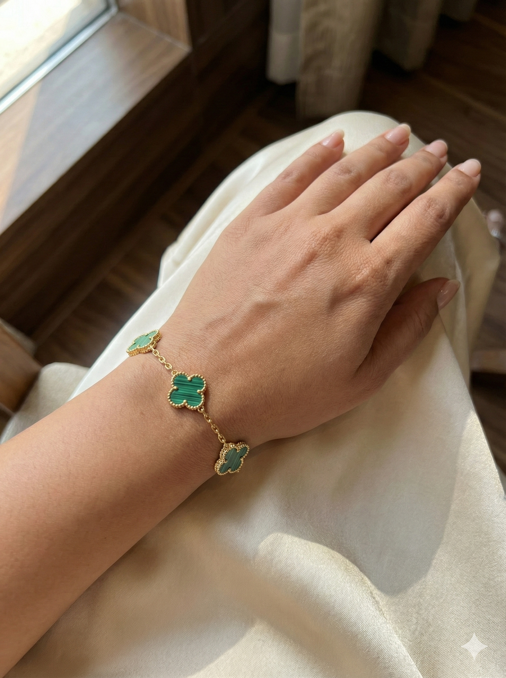 Close-up of a gold quatrefoil bracelet featuring striped green stone inlays and beaded edges