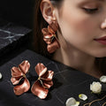 Close-up of rose gold textured metal flower earrings on green fabric