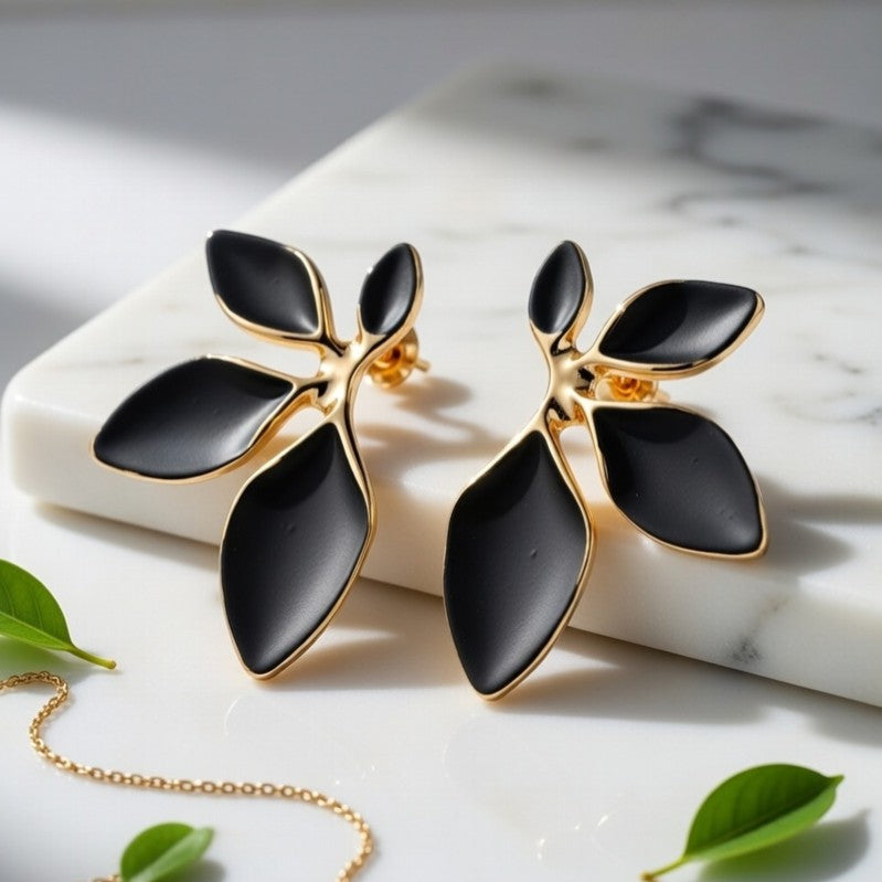 Matte black and gold leaf statement earrings on a marble surface