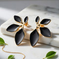 Matte black and gold leaf statement earrings on a marble surface