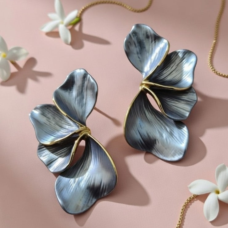 Pair of unique fan-shaped metal earrings with gold trim on pink velvet