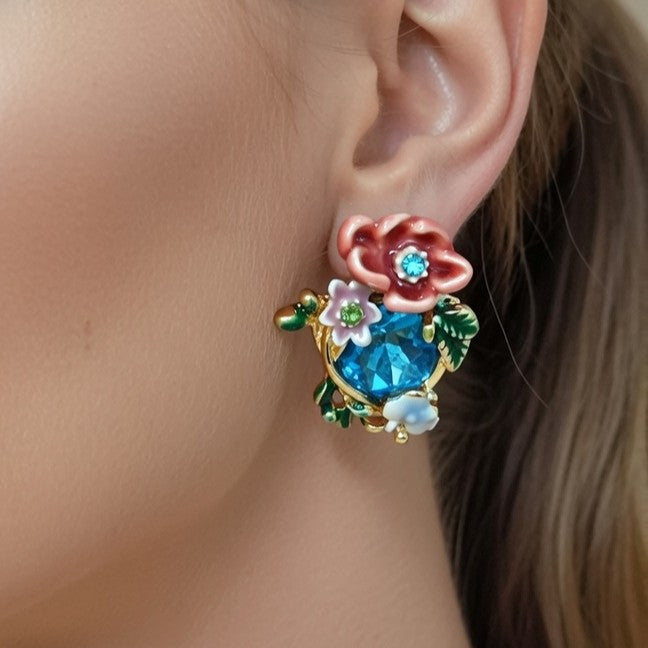 Vibrant garden-themed earrings showcasing a mix of Meenakari-style enamel work and bright blue gemstones. The design includes layered peach roses and small white wildflowers on a gold base